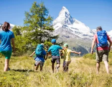 Familie mit drei Kindern wandert durch eine sonnige Alpwiese Richtung Matterhorn, Angebot Back to Nature rund um Zermatt.