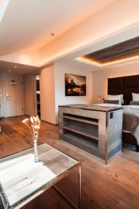 Junior Suite Chic mit Doppelbett, beleuchtetem Kopfteil, Kamin und Couchtisch aus Glas, Wohn-Schlafbereich im Hotel Bellerive Zermatt.