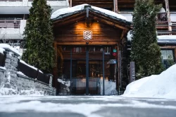 Verschneiter Holzeingang mit Glastüren, Tannen und Bellerive-Schild im Winter am Hotel Bellerive Zermatt.