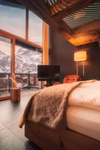 Sky Room mit weissem Bett, roten Sesseln und beleuchteter Holztreppe; durch die Glasfront Matterhorn im Abendlicht, Hotel Bellerive Zermatt.