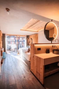 Offener Waschplatz mit rundem Spiegel, Holzgarderobe und Bett zum Balkon im Panorama Deluxe Room.
