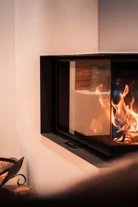 Eckkamin mit Flammen, Holzstapel und Kerzenhaltern im Luxus-Duplex-Apartment des Hotel Bellerive Zermatt.