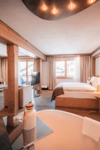 Junior Suite mit Sofa, Sessel, Bett in Holznische und Badewanne im Vordergrund, Blick zum Balkon, Hotel Bellerive Zermatt.